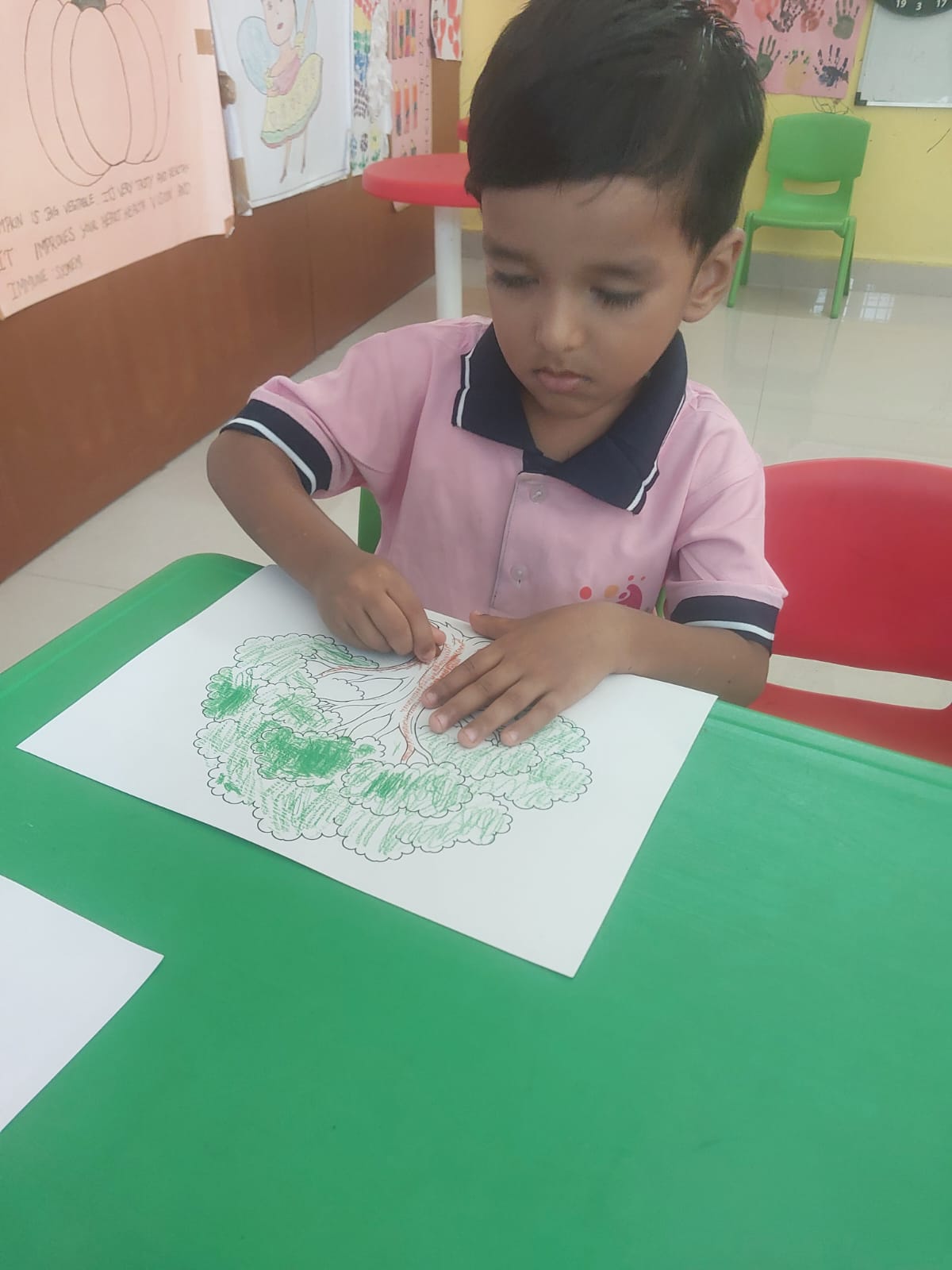 Child coloring a tree drawing with green crayon